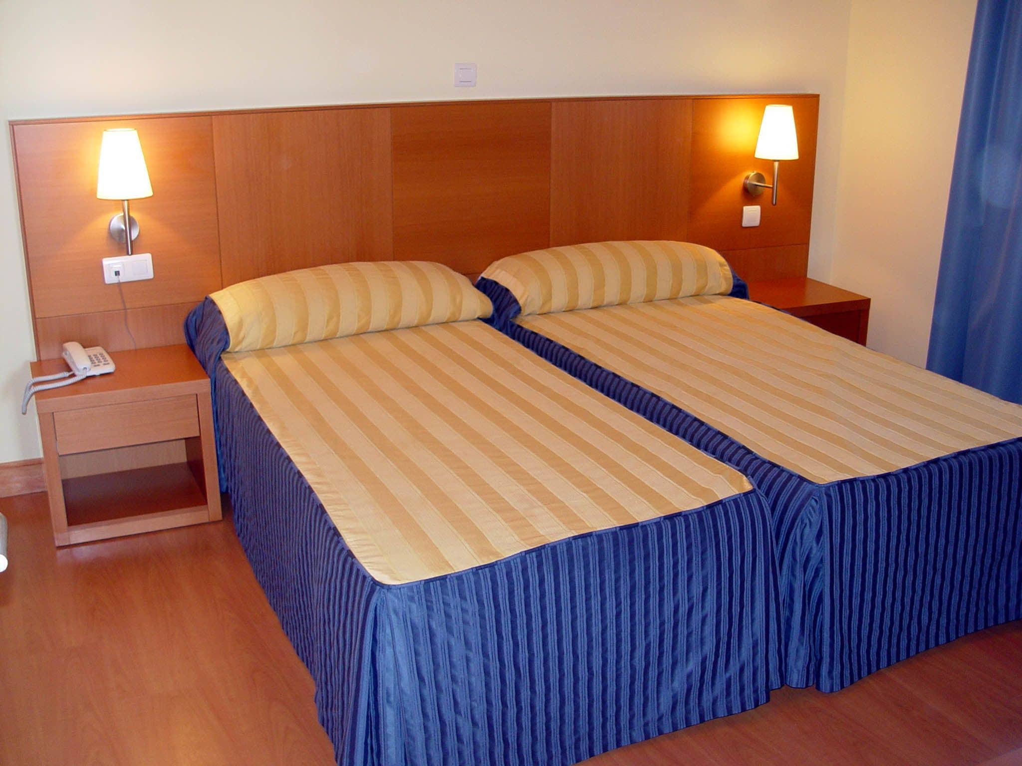 Una cama doble con ropa de cama a rayas, dos lámparas de noche, un teléfono en la mesita y un cabecero de madera.