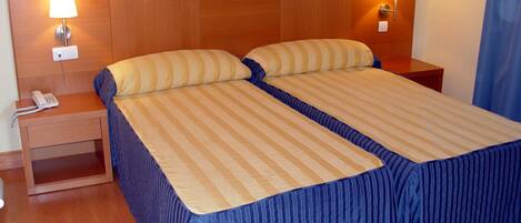 Una cama doble con ropa de cama a rayas, dos lámparas de noche, un teléfono en la mesita y un cabecero de madera.