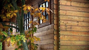 A rustic wooden building with large windows and a tree with autumn leaves in front. - Hotel Ibaigune (Murueta)
