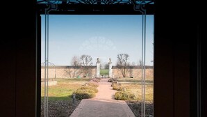 Blick durch eine Tür auf einen Weg zu einem Gebäude, strahlend blauer Himmel.