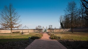 Ein Weg, der zu einem verschlossenen Eingang mit einer Backsteinmauer und Bäumen an beiden Seiten führt.