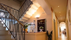 Eine Hotelhalle mit Treppe, einer Rezeption und einem Flur zu den Zimmern.