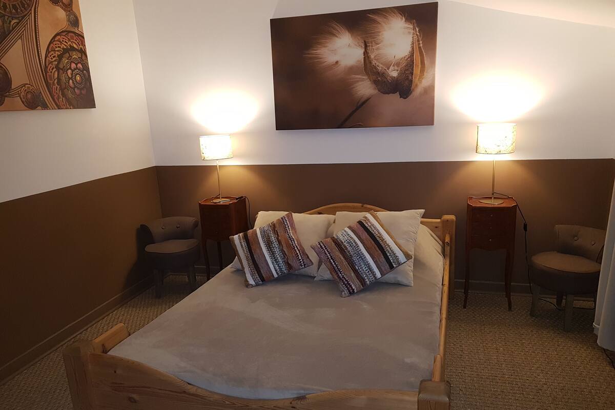 Un dormitorio ordenado con una cama de madera, dos lámparas de noche, una obra de arte en la pared y dos sillas.