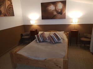 Un dormitorio ordenado con una cama de madera, dos lámparas de noche, una obra de arte en la pared y dos sillas.