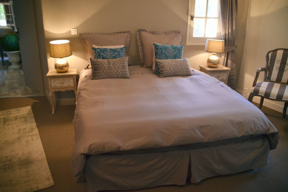 Una cama grande con muchas almohadas, dos lámparas de noche y una silla.