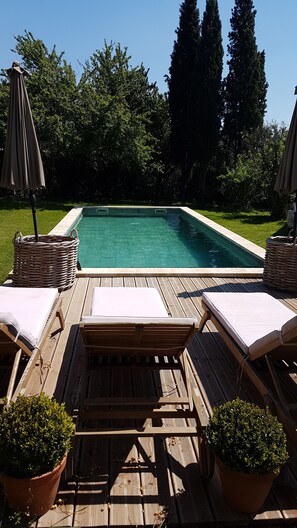 Una terraza de madera con sillones de descanso y una piscina.