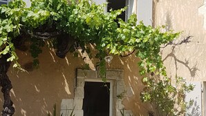 A building with a rustic facade, a gravel courtyard, and potted plants. - Mas Roussillon (Roussillon)
