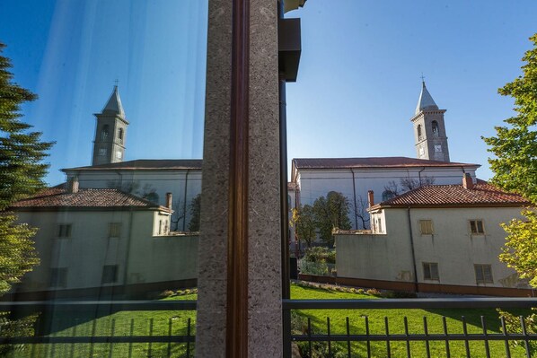 A building with two towers and a central section, surrounded by a green lawn and a fence. - Center Hotel (Trieste)
