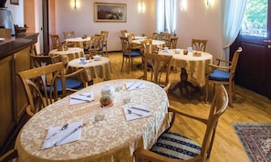 A dining area with round tables, wooden chairs, and a patterned tablecloth.