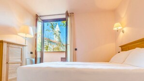 Habitación de hotel con cama, ventana con cortinas, lámpara y vista a un edificio.