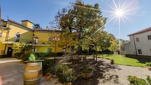 Une cour avec un grand arbre, un tonneau en bois et un bâtiment doté d’un balcon.