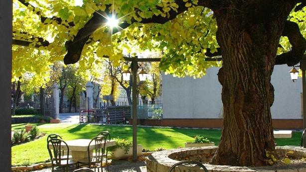 Une terrasse extérieure avec une table et des chaises en pierre, entourée d’un grand arbre et d’un lampadaire.
