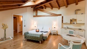 Une chambre avec un lit, des tables de chevet, un petit bureau et un coin cuisine.