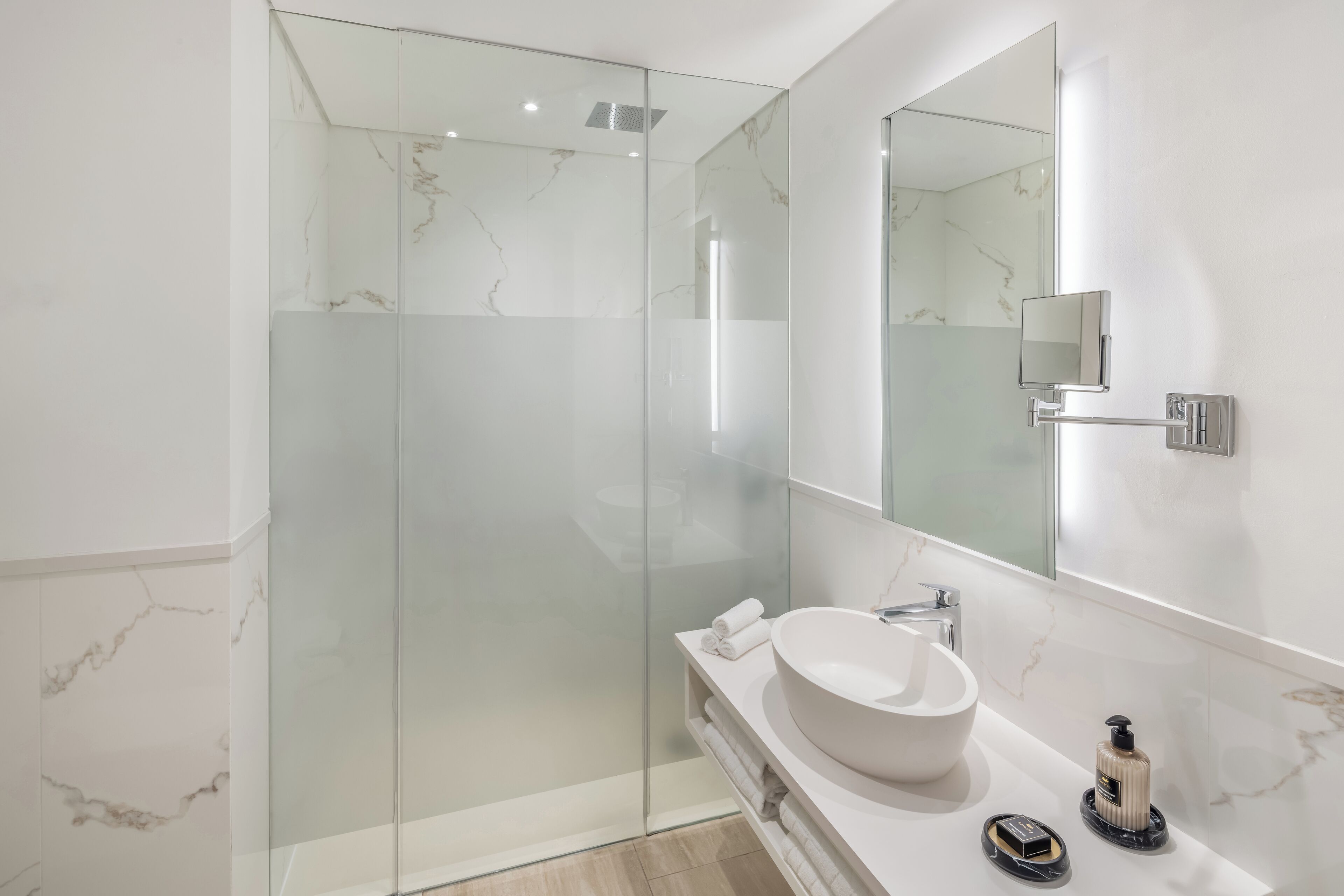 A modern bathroom with a glass-enclosed shower, a large mirror, and a white marble countertop.