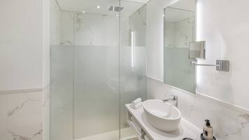 Un baño moderno con ducha de vidrio, un espejo grande y una encimera de mármol blanco.