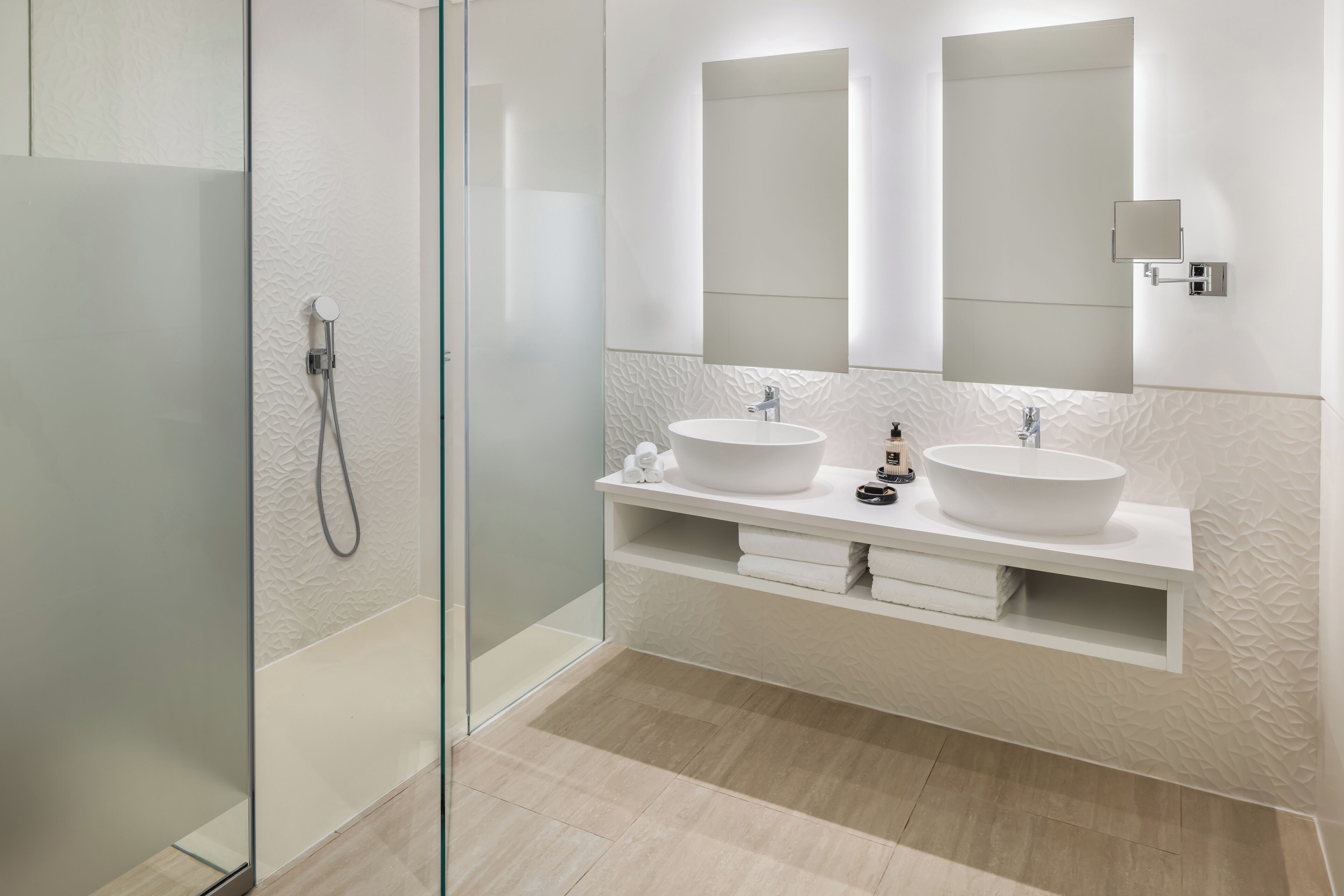 A modern bathroom with two sinks, a glass shower enclosure, and a large mirror.