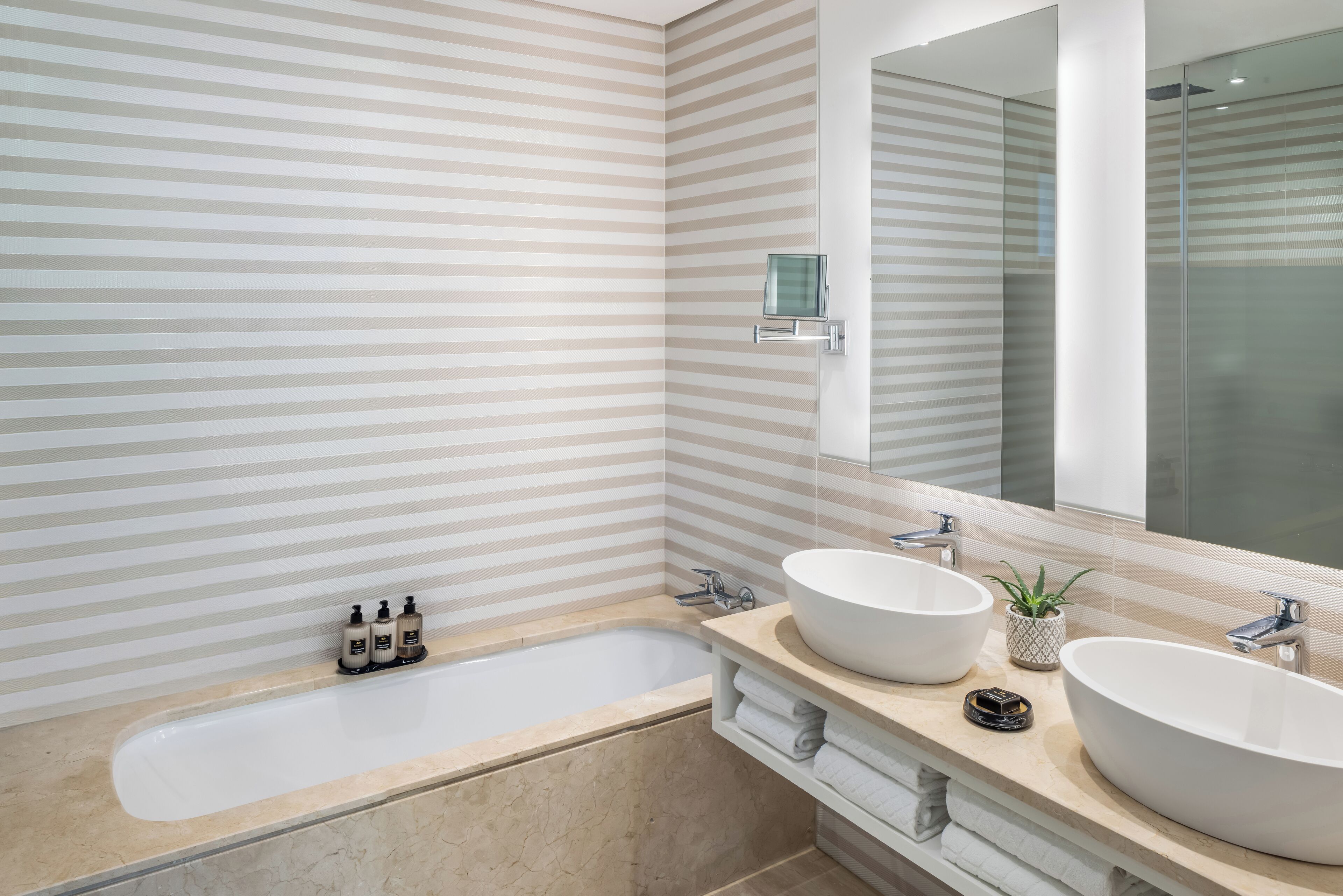 A modern bathroom with striped walls, a large bathtub, two sinks, and a mirror.