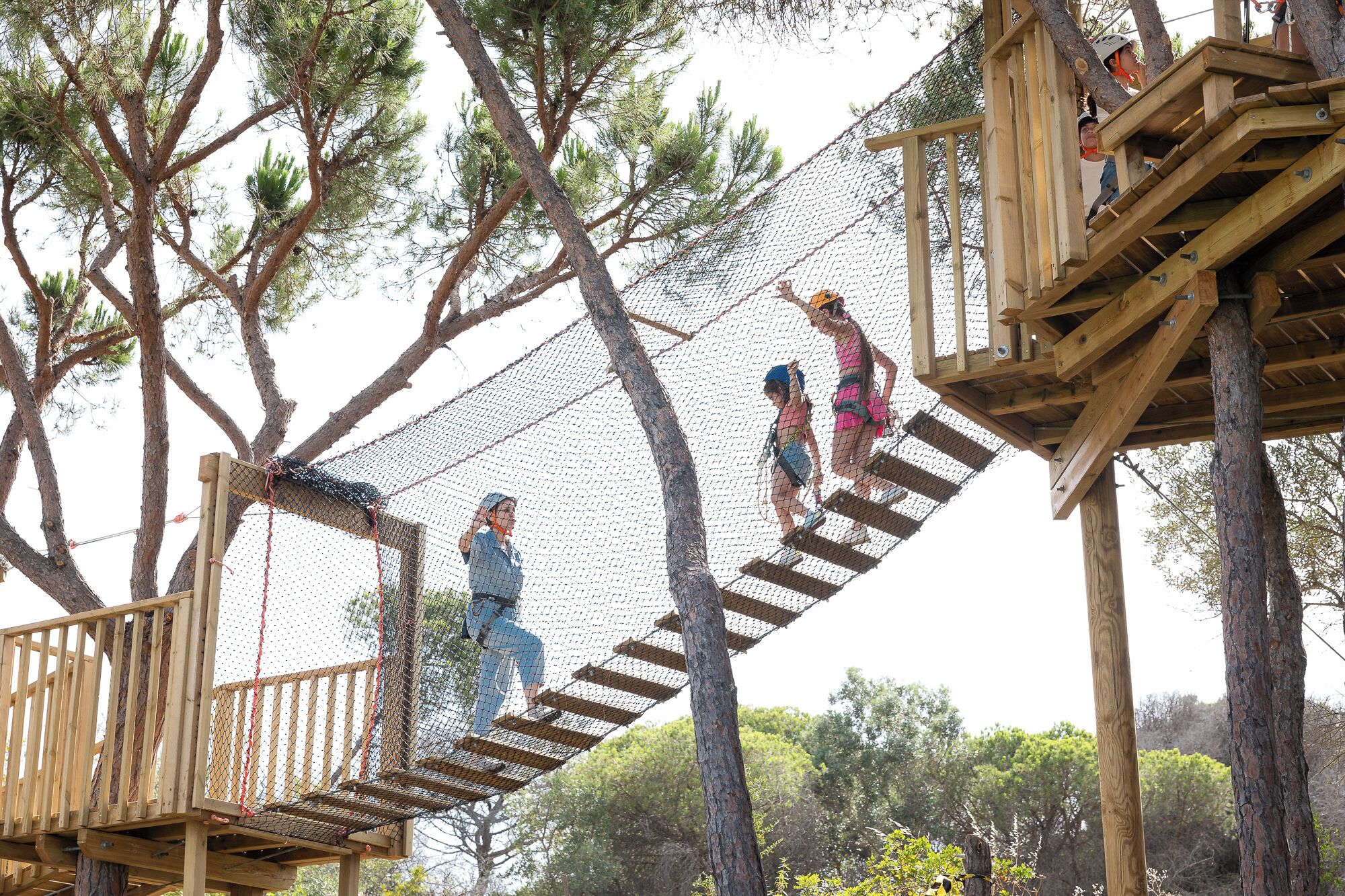 A wooden rope bridge over a netted obstacle course in a wooded area.