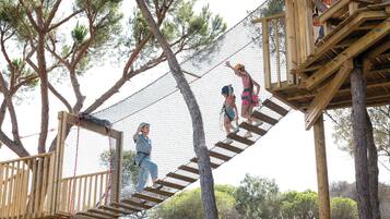 A wooden rope bridge over a netted obstacle course in a wooded area.