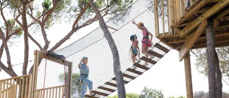 A wooden rope bridge over a netted obstacle course in a wooded area.