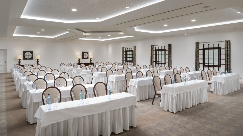 Ein großer Konferenzraum mit Tischen und Stühlen, ausgestattet mit Wasserflaschen und Gläsern.
