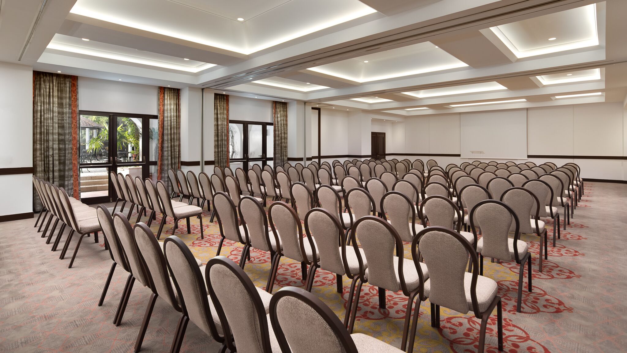 A large conference room with rows of chairs, a stage with a projector, and large windows with curtains.