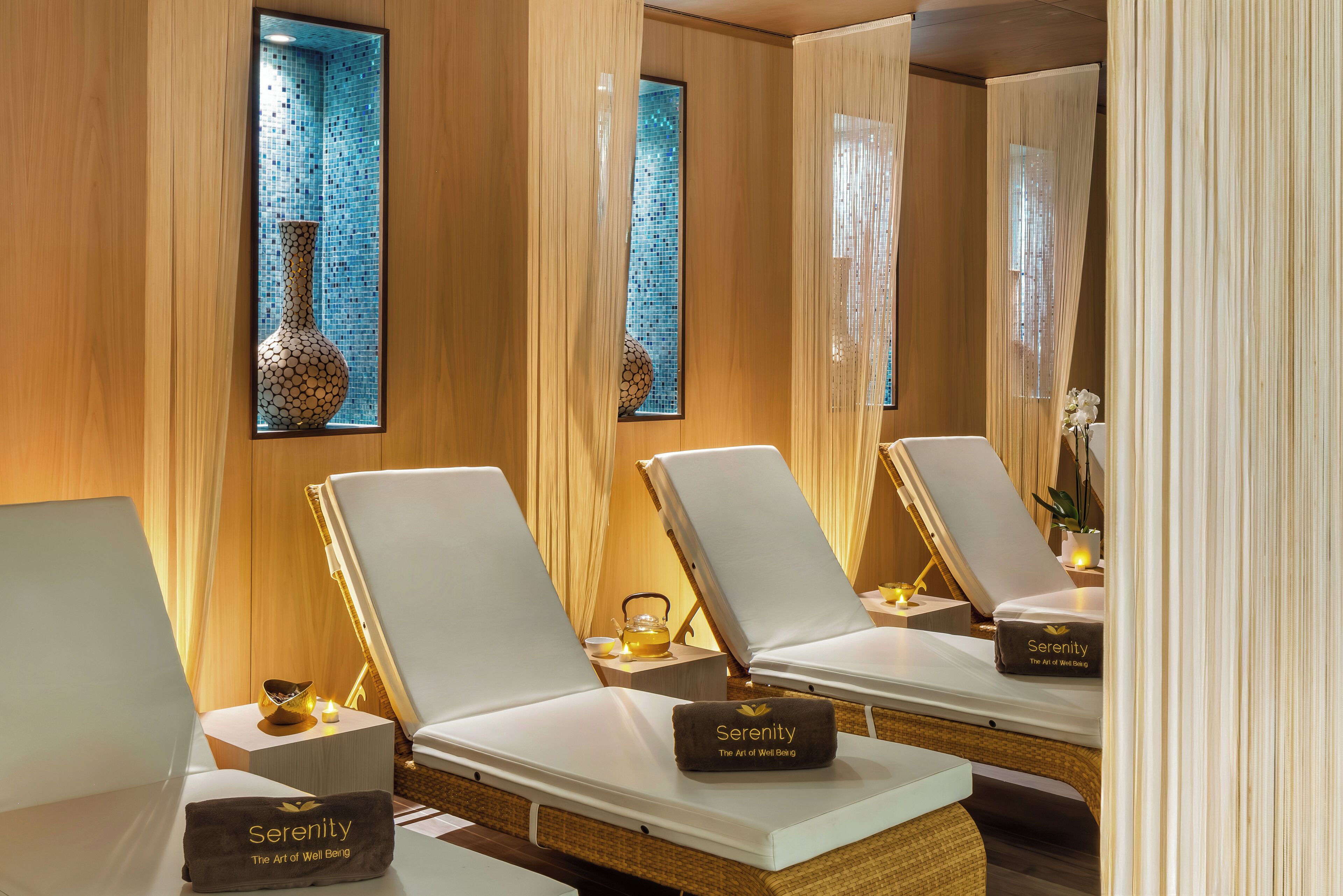A spa room with three white lounge chairs, each with a small table and a 'Serenity' branded item.