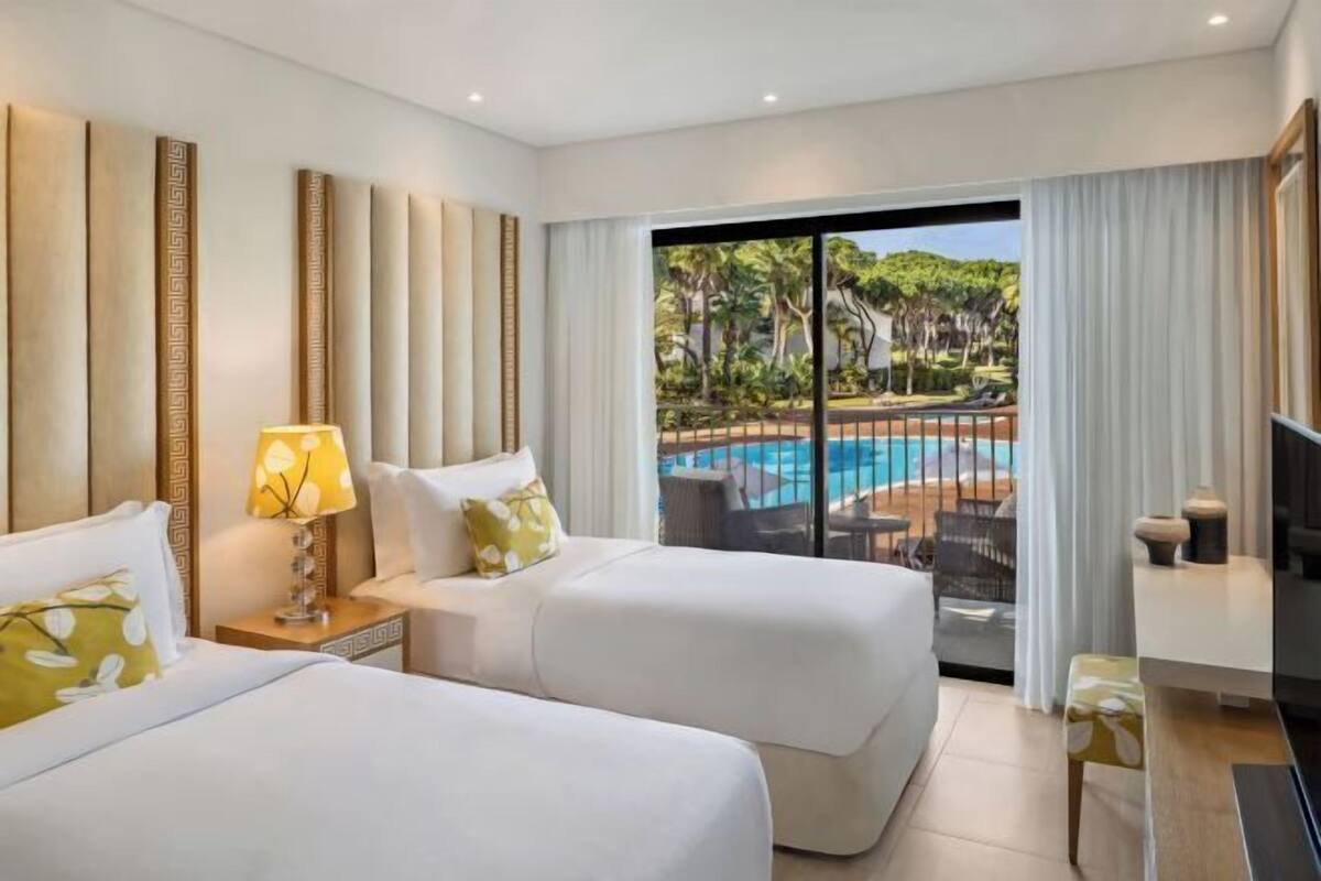 Une chambre d’hôtel avec deux lits, une télévision et une vue sur une piscine.