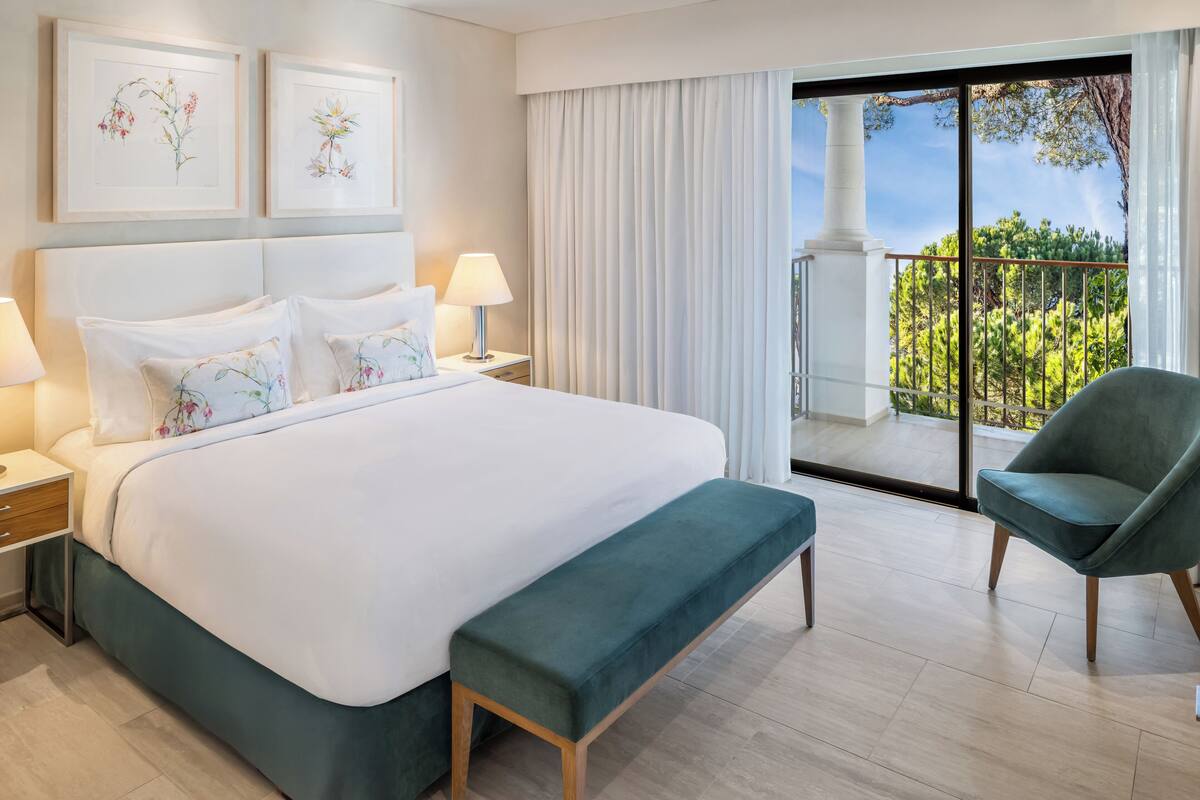 Une chambre d’hôtel avec un grand lit, un banc, une chaise et un balcon avec vue.