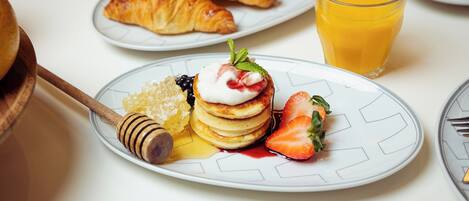 Une assiette de petit-déjeuner avec des crêpes, des fraises, du miel et un croissant.