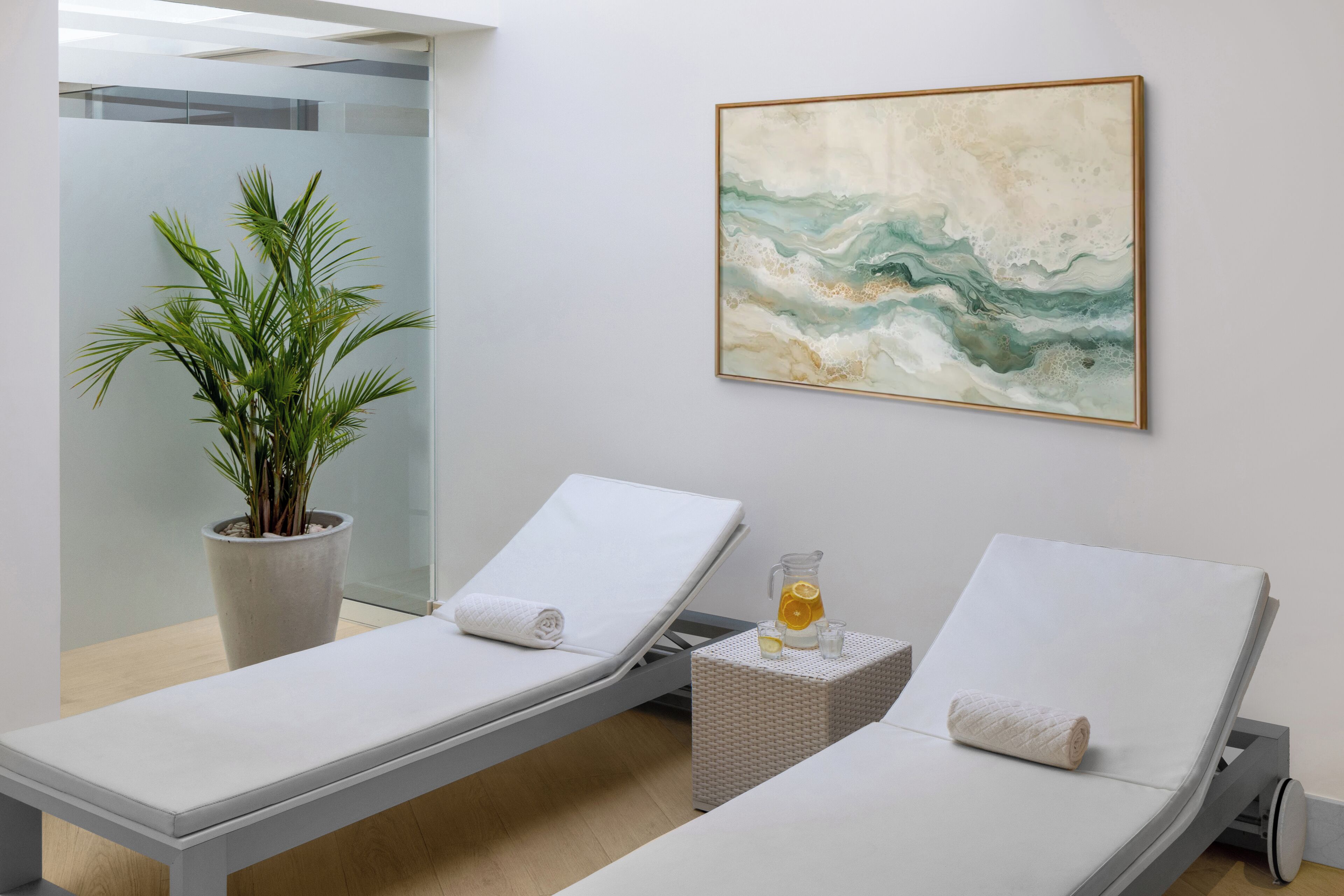 A spa room with two reclining chairs, a potted plant, a painting, and a small table with a pitcher and glasses.