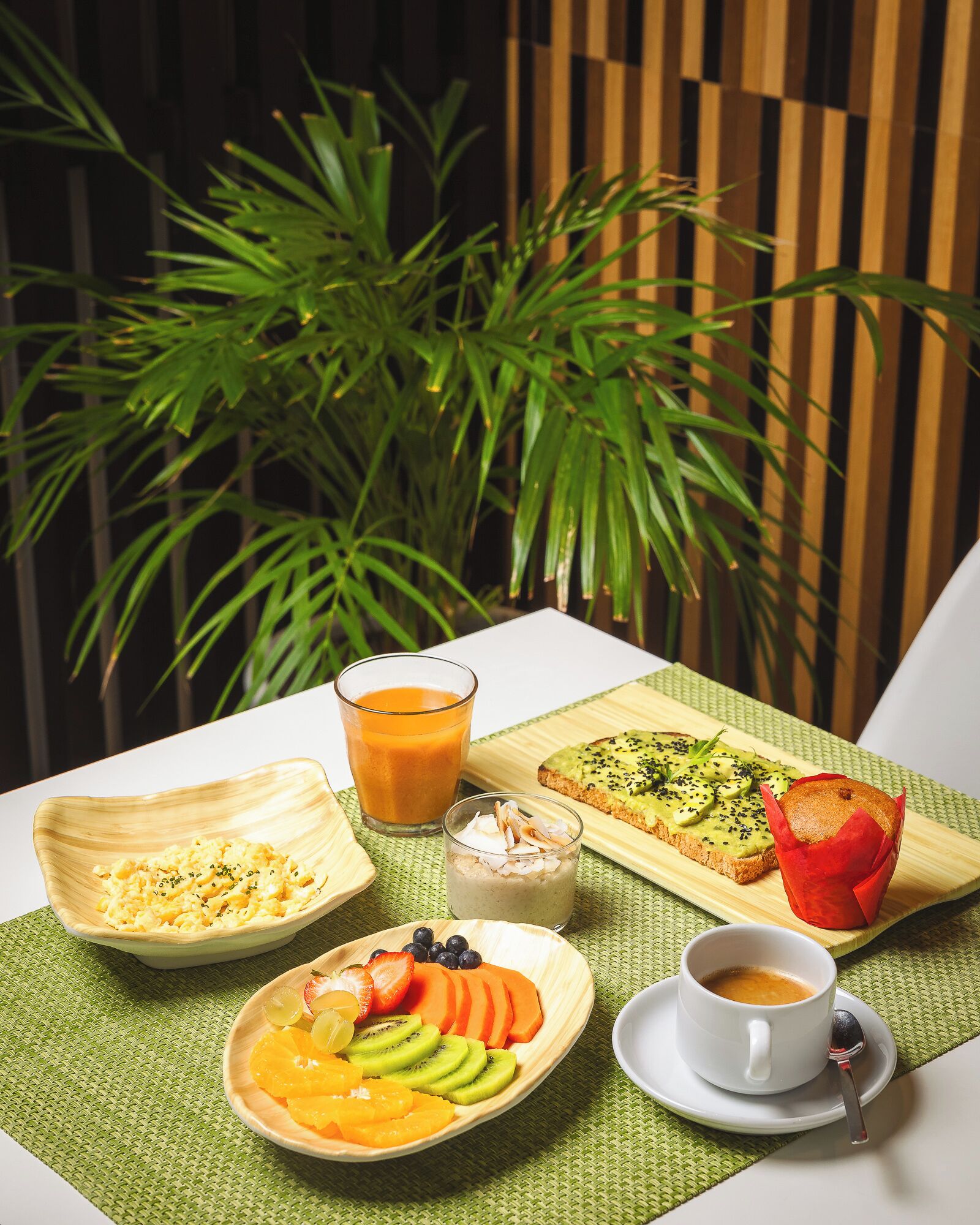 A table with breakfast items including scrambled eggs, a smoothie, avocado toast, a muffin, and a fruit bowl.