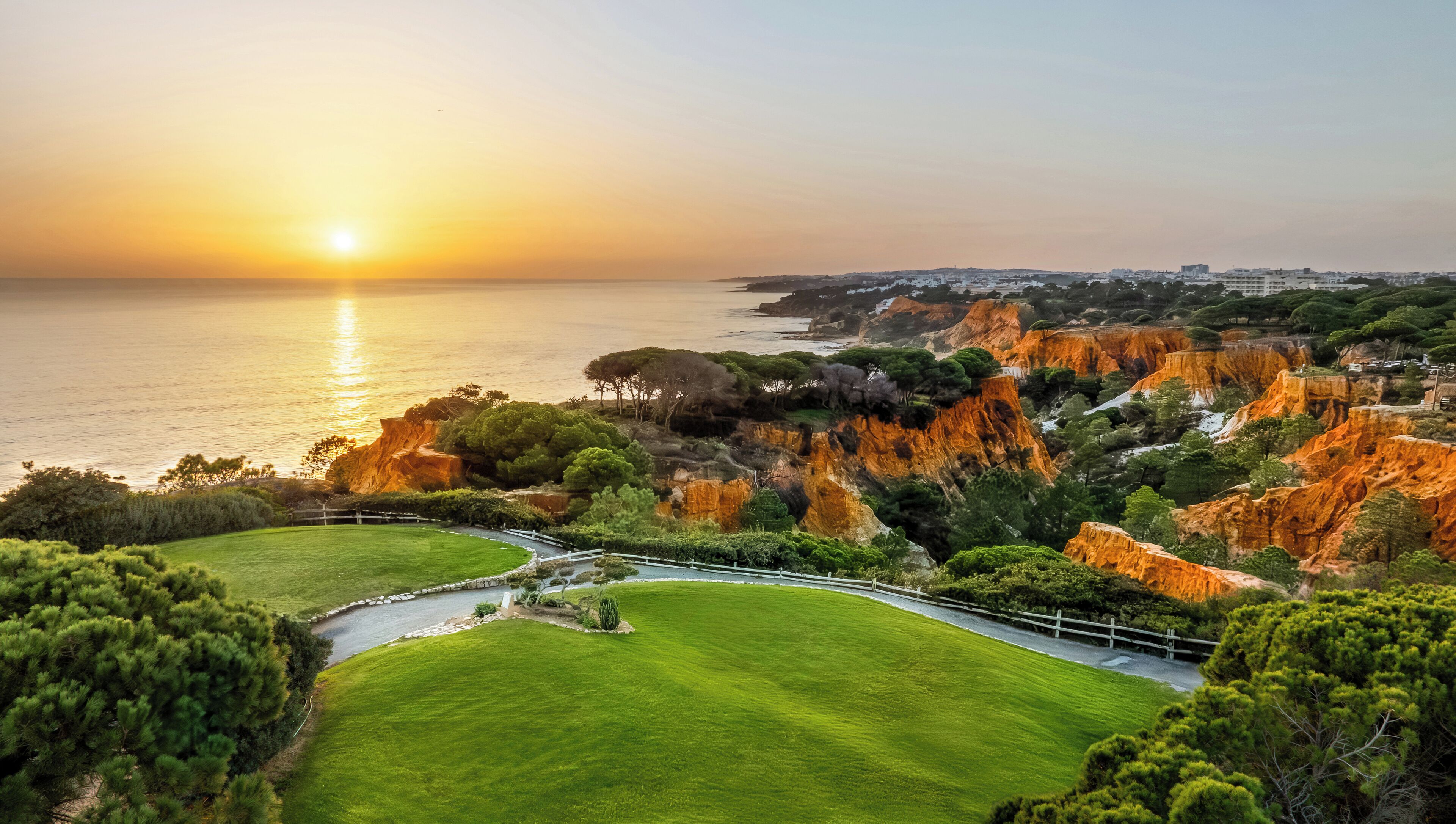 A coastal landscape with a grassy area, a winding path, and rocky cliffs.