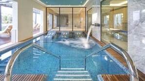 Une piscine intérieure moderne avec des parois en verre transparent, une terrasse en bois et un mur en marbre.