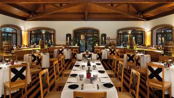 A restaurant with a long table set for a meal, wooden chairs, and a high ceiling with exposed beams.