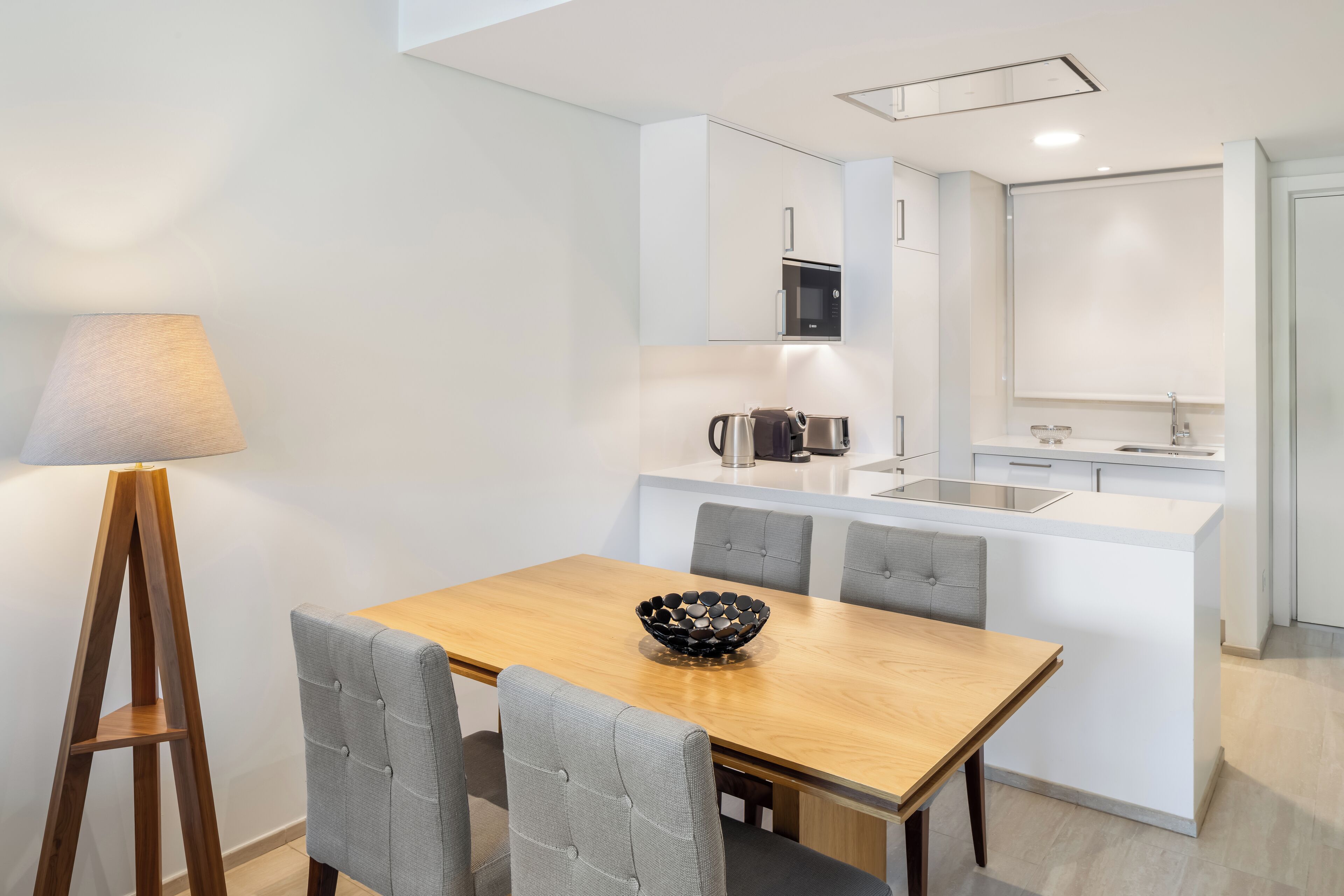 A modern kitchen with white cabinetry, a central island, and a dining area with a wooden table and grey upholstered chairs.
