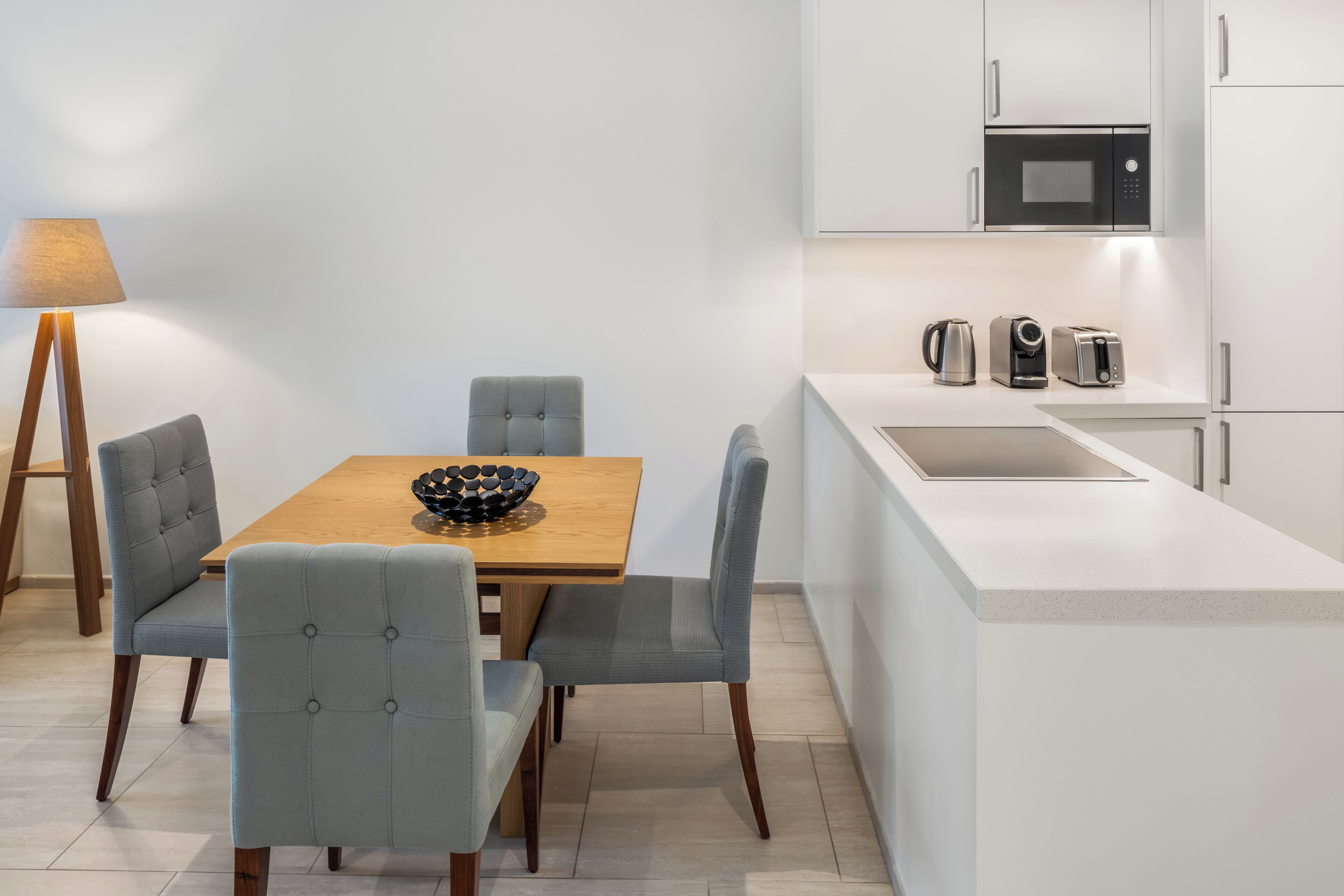 Una cocina moderna con una mesa de comedor de madera, sillas grises tapizadas, un bol negro y una lámpara.