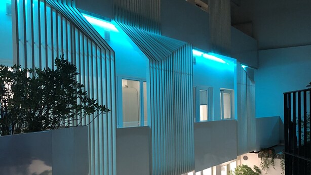 Un edificio moderno con fachada de vidrio, listones verticales y un interior iluminado en azul.