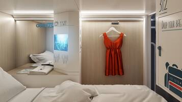 A hotel room with a bed, a hanging red dress, a screen displaying a cityscape, and a door with a number.