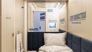 Una habitación de hotel compacta con una cama, una mesita de noche pequeña y un televisor montado en la pared.