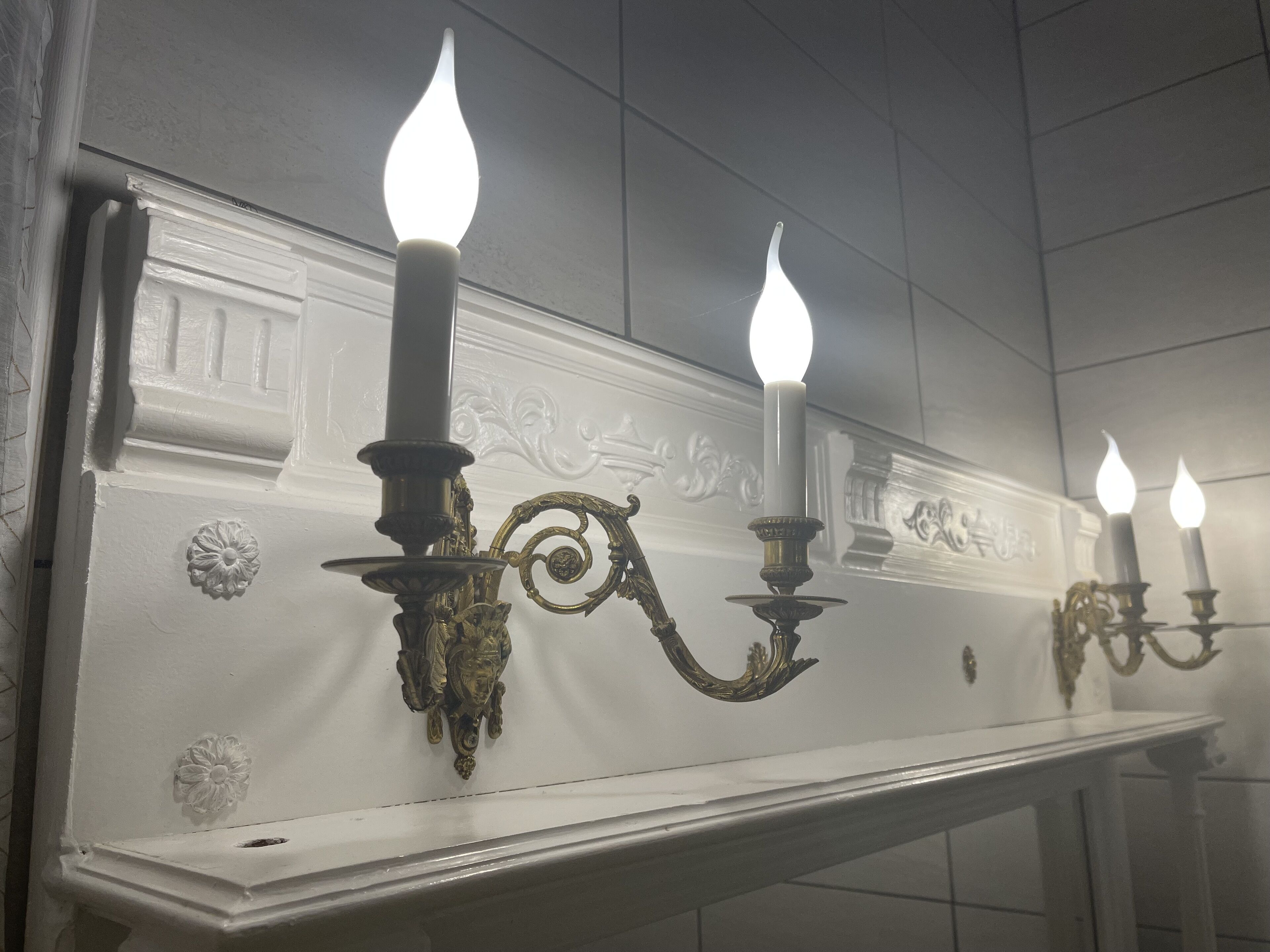 A white wall with three ornate wall sconces with candles, each featuring a curved design and a central flame.