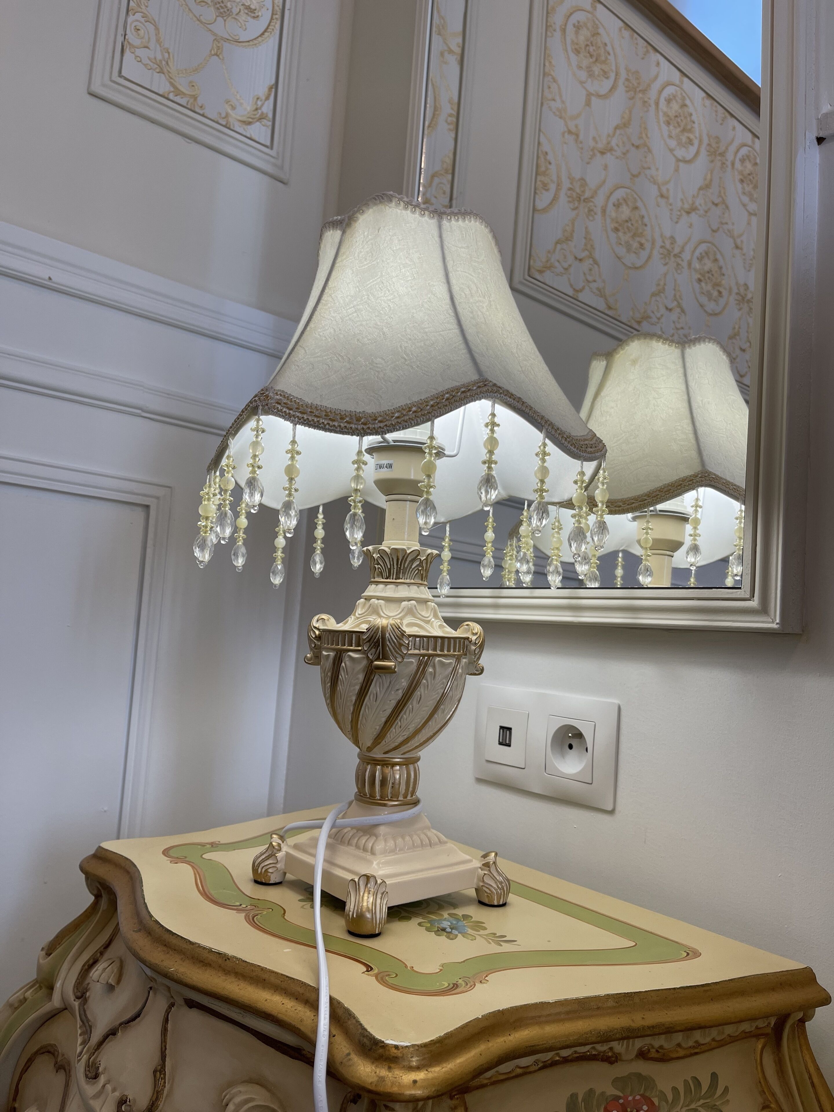 Una lámpara decorativa con pantalla blanca y cuentas de cristal sobre una mesa con intrincados relieves.