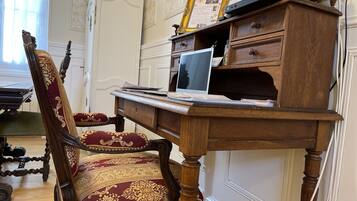 A wooden desk with a laptop, a framed certificate, and a wooden chair with a red and gold patterned upholstery.