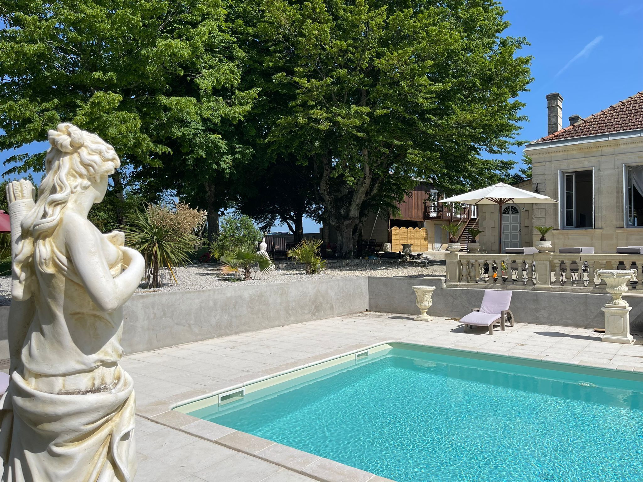 Ein Schwimmbecken mit Statue, Liegestühlen und einem Gebäude mit einem Ziegeldach.