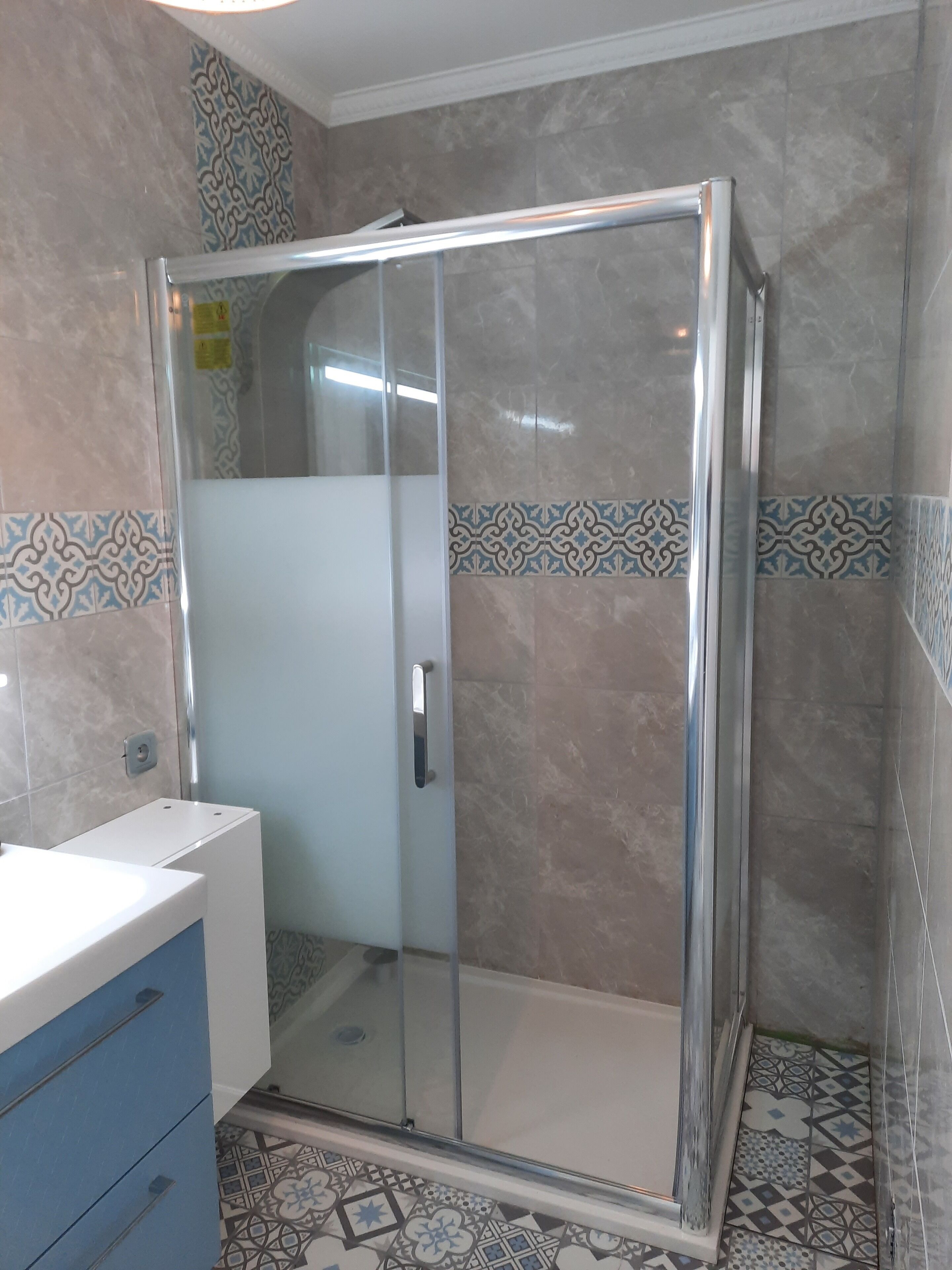 A bathroom with a glass-enclosed shower, a white sink, and patterned tiles on the walls and floor.