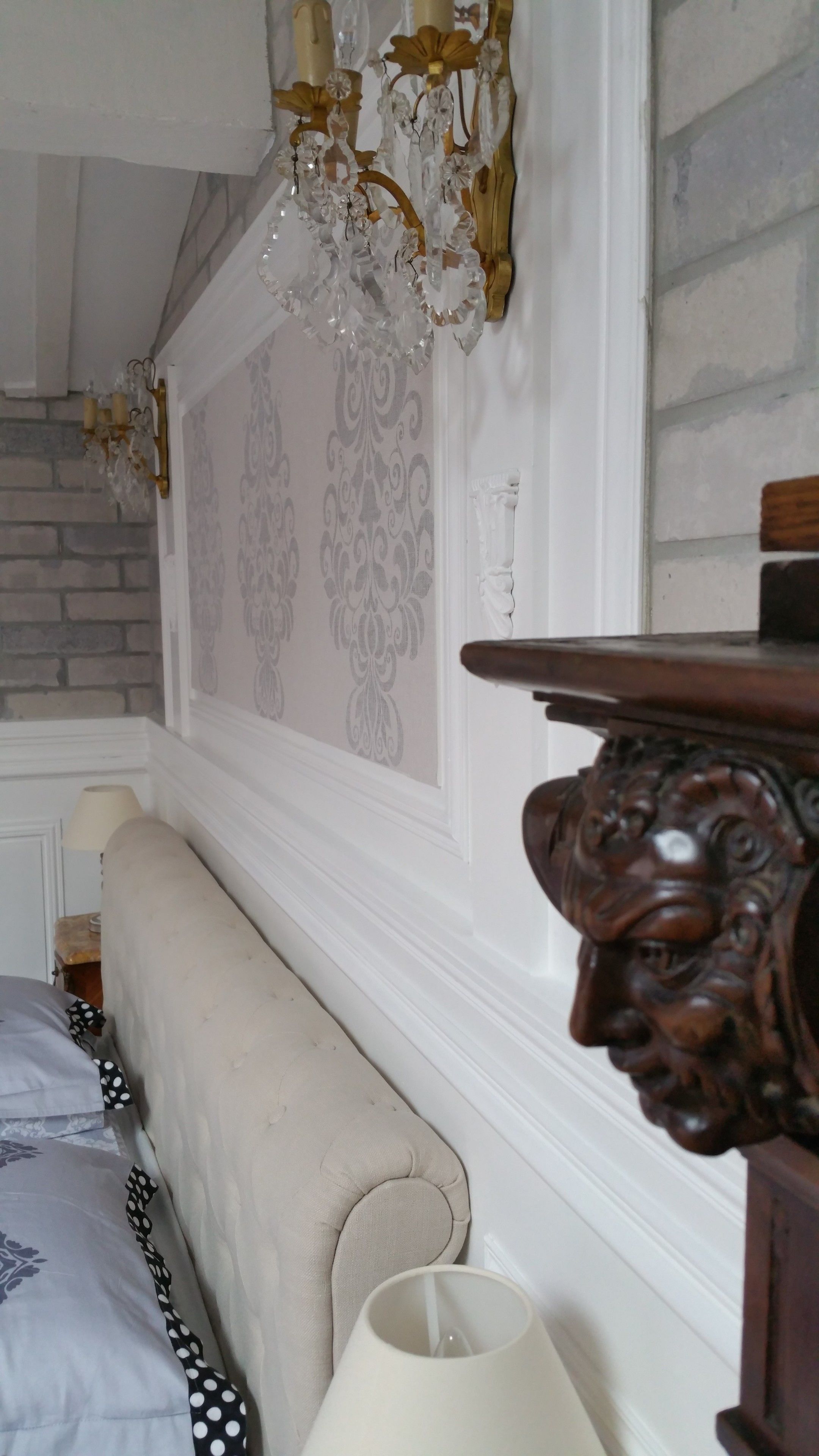 Quarto com cama, lustre, cabeceira de madeira e papel de parede estampado.