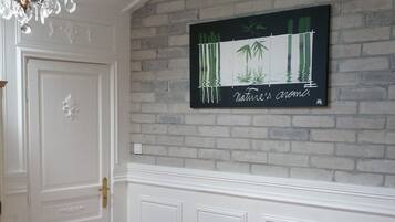 Une pièce avec une porte blanche, un bureau en bois avec une chaise, un lustre et un tableau représentant des bambous accroché au mur.