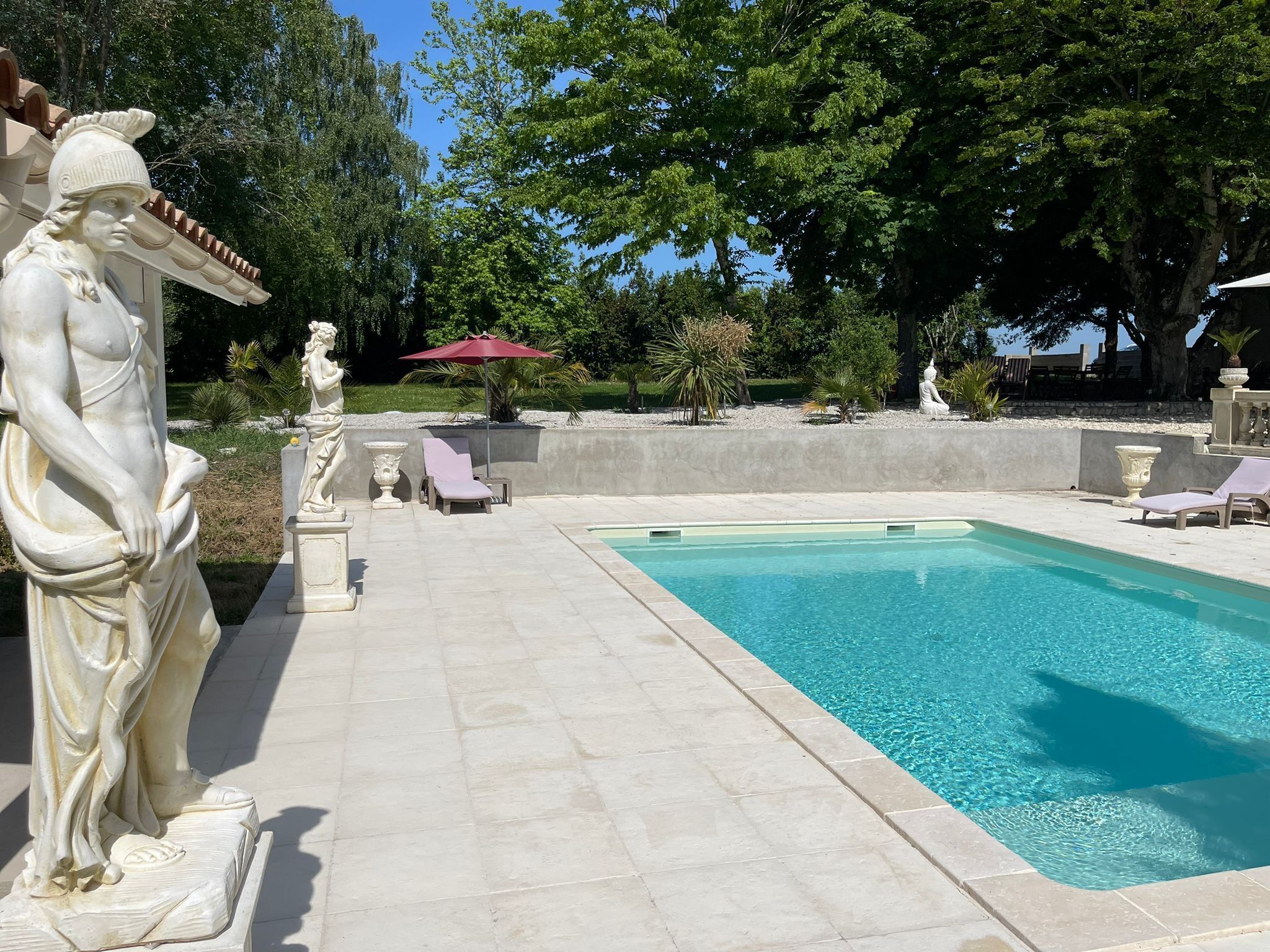 A pool area with statues, lounge chairs, and a red umbrella.