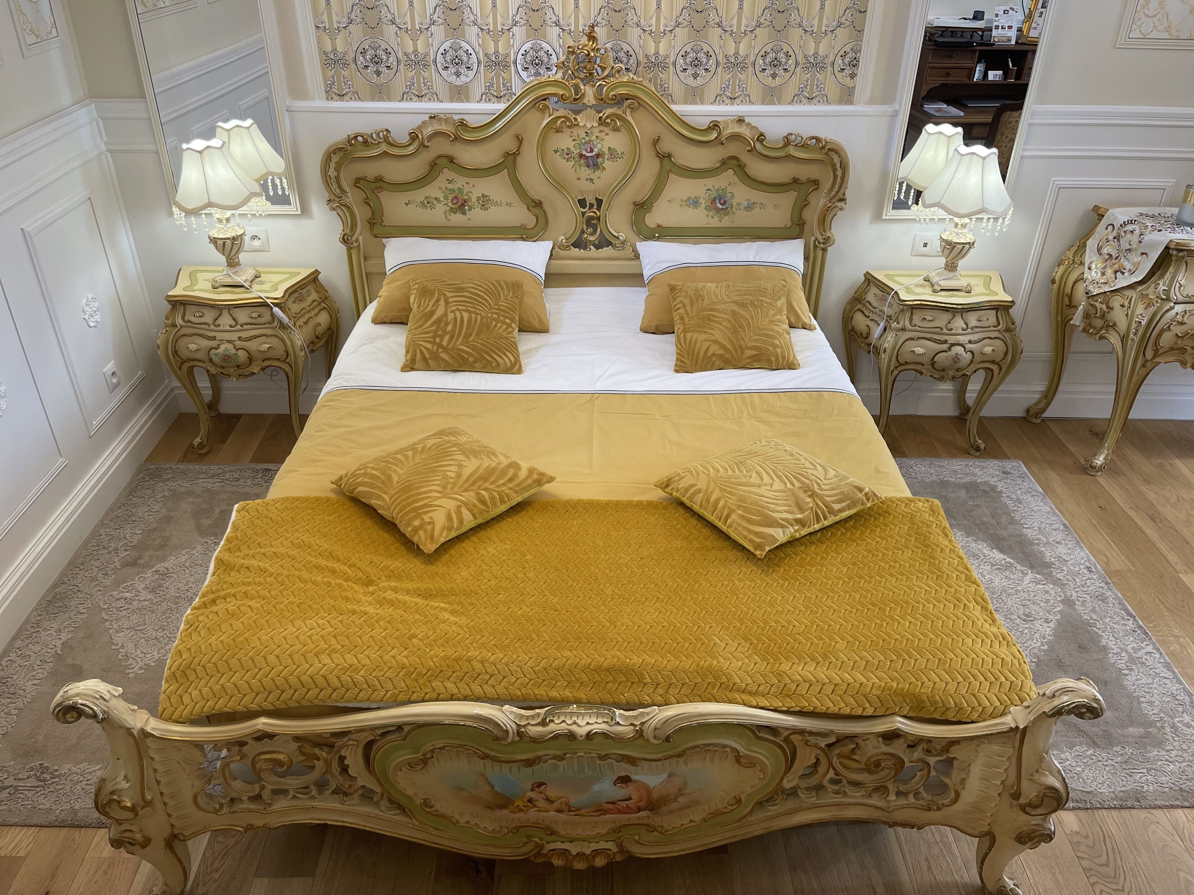 Una cama grande con dos mesas de noche a cada lado, con lámparas, y cabecera y piecera decorados.