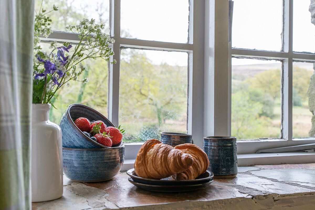 A rustic breakfast setup with croissants, strawberries, and a vase of flowers by a window.